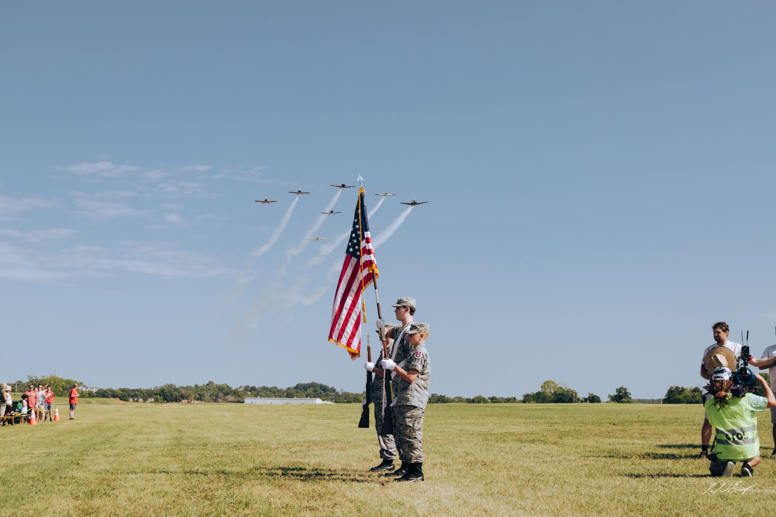 Color guard salute under a smoke-trail formation flyover