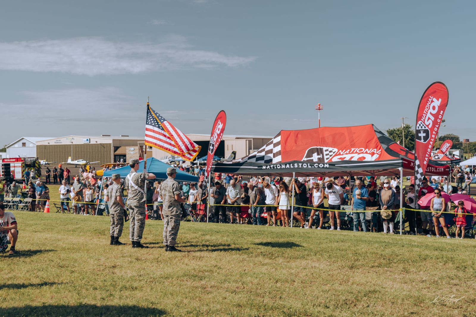 Color guard presenting the flags along a packed fence line