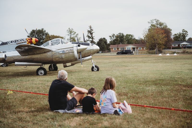 A family picnics on the grass beside the P-38 replica